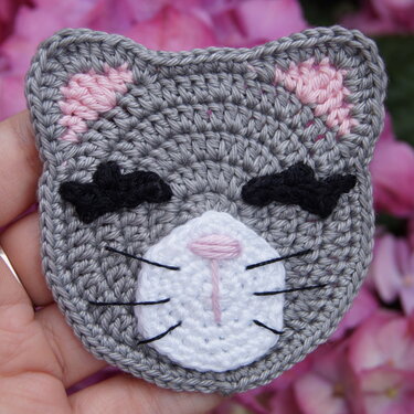 Gehäkelte graue Katzen-Applikation mit weißer Schnauze, rosa Innenohren und schwarzen Stickdetails