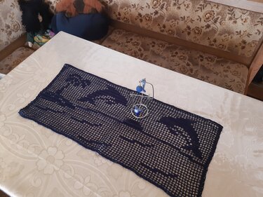 Dunkelblauer gehäkelter Tischläufer im Filetmuster mit Delfinmotiv auf hellem Tisch