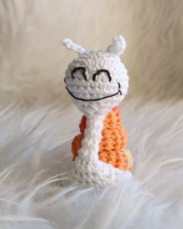 Weiß‑orange gehäkelte Amigurumi‑Schnecke mit aufgesticktem Lächeln