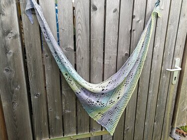 Gestricktes Dreieckstuch in Blau, Lila, Türkis und Hellgrün mit Lochmuster, an einem Holztor hängend