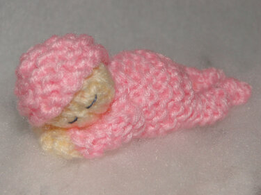 Tiny pink knitted amigurumi baby wrapped in a swaddle