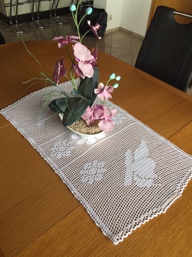 Weißer gehäkelter Tischläufer auf Holztisch mit rosa-lila Orchidee und Hasenmuster