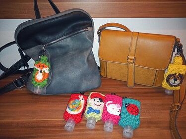 Mehrere bunte, gehäkelte Flaschenhüllen als Taschenanhänger; zwei Hüllen sind an Lederhandtaschen befestigt