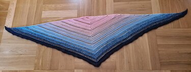 Gehäkeltes Dreieckstuch mit rosa‑blauem Farbverlauf auf Parkettboden