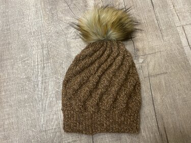 braune gestrickte Beanie mit großem Bommel auf Holzfußboden