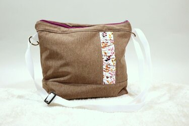 Braune Stoff-Umhängetasche mit weißem Gurt, Blättermotiv-Zierstreifen und violettem Reißverschluss