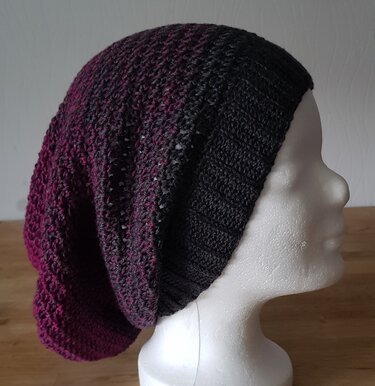 Gehäkelte Longbeanie mit Farbverlauf von Schwarz zu Magenta auf einem weißen Schaufensterpuppenkopf.