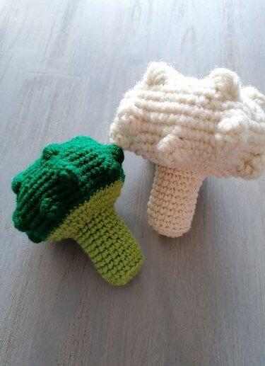 Gehäkelter grüner Brokkoli und weißer Blumenkohl auf hellem Holz