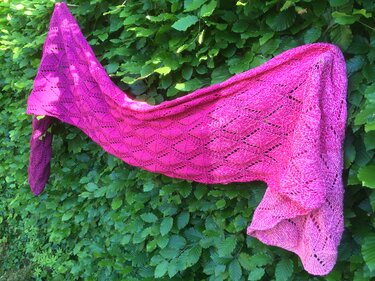Asymmetrisches gestricktes Dreieckstuch in Pink mit Ajour-Blattmuster an grüner Hecke