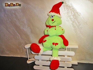 Grünes gehäkeltes Amigurumi mit roter Weihnachtsmütze auf weißem Schlitten
