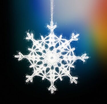 Weiße gehäkelte Schneeflocke vor farbigem Verlaufhintergrund.