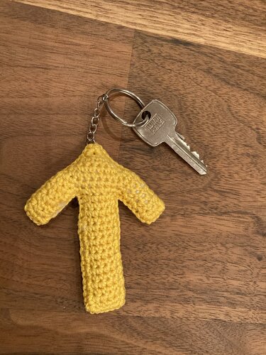 Gehäkelter gelber T‑förmiger Schlüsselanhänger auf Holztisch