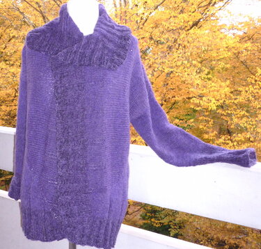 Lila gestrickte Damenjacke mit breitem geripptem Kragen auf Büste vor herbstlichem Laub