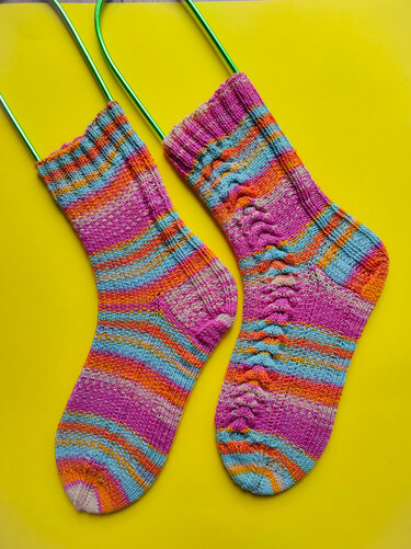 Paar handgestrickter bunter Streifensocken auf gelbem Hintergrund