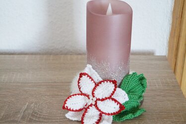 Gehäkelter weiß-roter Weihnachtsstern mit grünen Blättern und rosa LED-Kerze auf Holz