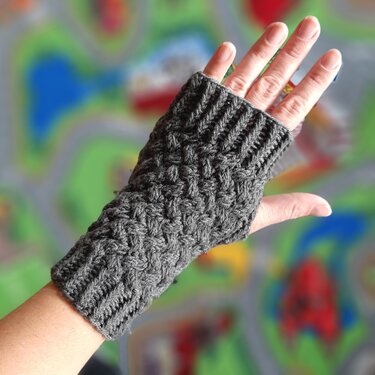 Grau gestrickte Armstulpe mit Zopfmuster an einer Hand