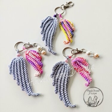 Anordnung gehäkelter Engelsflügel und bunter Mini-Mützen als Anhänger auf hellem Hintergrund