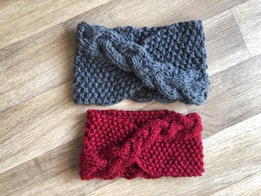 Zwei gestrickte Stirnbänder in Grau und Rot mit Zopfmuster auf Holzboden