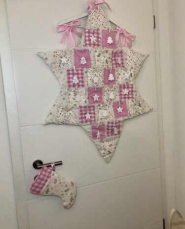 Gepatchter sternförmiger Adventskalender-Wandbehang in Rosa und Beige mit nummerierten Täschchen, weißen Holzanhängern und Stoffstiefel am Türgriff