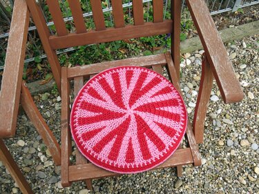 Rundes gehäkeltes Sitzkissen in Rot und Pink auf einem Holzstuhl