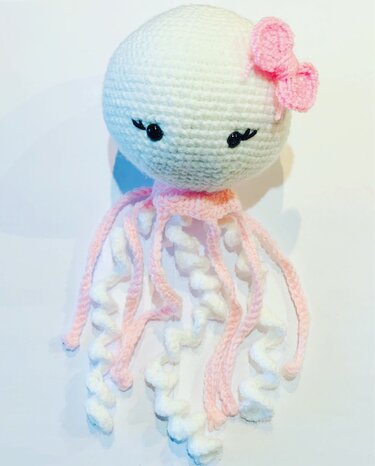 Weiße gehäkelte Amigurumi-Qualle mit rosa Schleife und detaillierten spiralförmigen Tentakeln