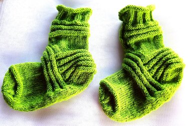 Zwei leuchtend grüne handgestrickte Socken mit Strukturmuster auf hellem Hintergrund