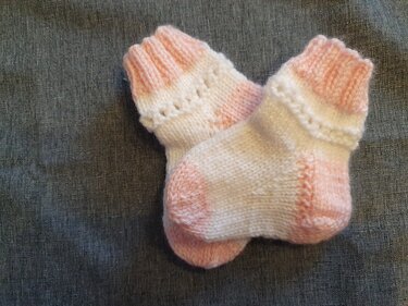 Paar gestrickter Babysocken in Rosa und Weiß mit Rippenbündchen auf grauem Stoff