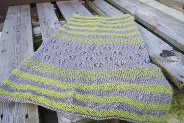 Gestrickter Schlauchschal in Grau und Lindgrün mit Streifen und Lochmuster auf Holzlatten.