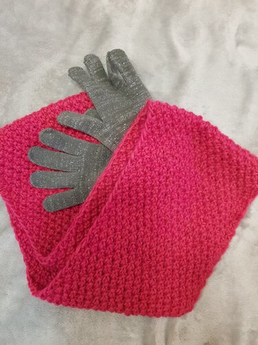 Gestrickter fuchsiafarbener Loopschal und graue Glitzerhandschuhe auf weißer Decke