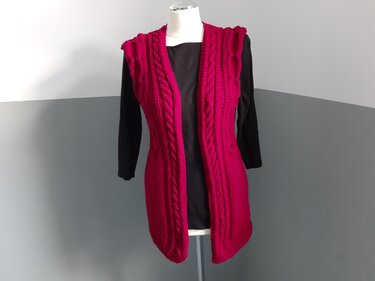 Lange ärmellose Strickweste in Magenta mit Zopfmuster auf Mannequin über schwarzem Langarmshirt