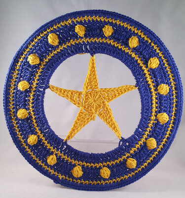 Runder gehäkelter Anhänger in Blau und Gelb mit gelbem fünfzackigem Stern in der Mitte