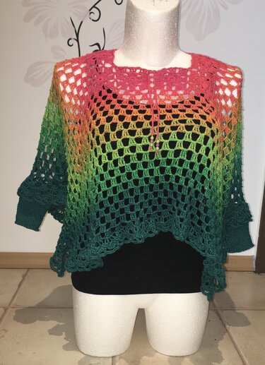 Gehäkelter Damenponcho auf Schaufensterpuppe mit Farbverlauf in Pink, Orange und Grün und offenem Quadrat-Lochmuster