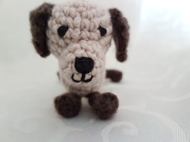 Nahaufnahme eines kleinen gehäkelten Hundeamigurumi mit sichtbaren Maschen und gestickter Nase