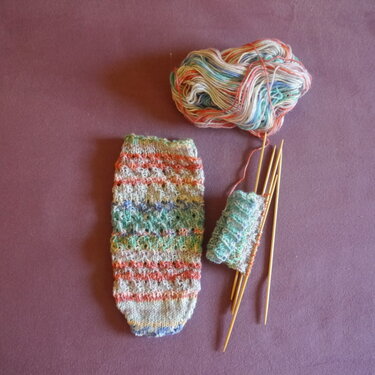 Mehrfarbige gestrickte Socke, angefangenes Strickstück, Bambus-Doppelspitznadeln und Knäuel auf violettem Untergrund