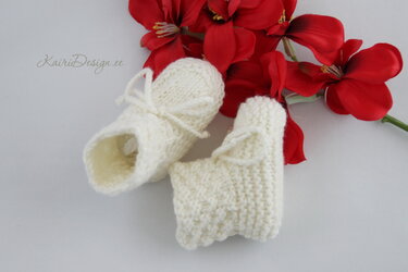 Cream hand-knit baby booties with tie cords beside red flowers