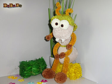Gehäkelte Amigurumi‑Raupe sitzt mit grüner Mütze und großen Augen