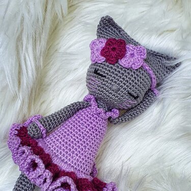 Graue gehäkelte Amigurumi-Katze mit lila Rüschenkleid und Blumen-Stirnband