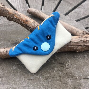Kleiner Filzbeutel aus Filz mit blauer, tierförmiger Klappe, gestickten Augen und hellblauem Druckknopf auf Holzuntergrund.