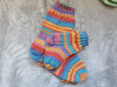Gestreifte Ringelsocken in Baby- und Damengröße auf hellgrauem Stoff