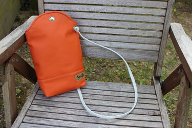 Kleine orangefarbene Tasche mit Zugband und Druckknopf auf einem Holzstuhl