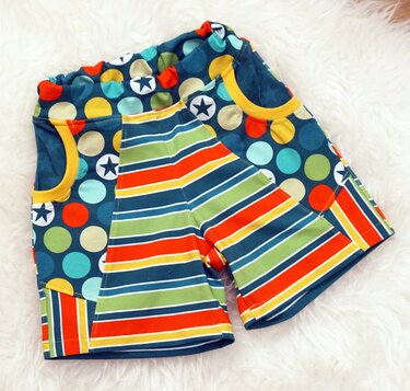 Nahaufnahme von Kinder-Shorts mit elastischem Bund, Seitentaschen und buntem Muster aus Punkten, Sternen und Streifen.