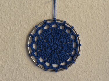 Blauer gehäkelter Traumfänger mit Metallring an heller Wand