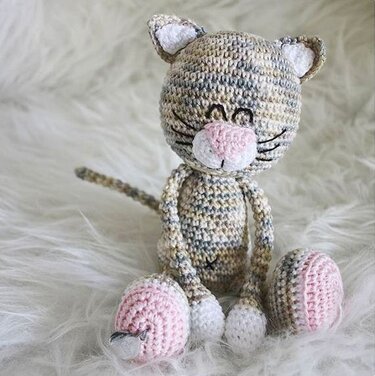 Gehäkelte Amigurumi-Katze aus meliertem Garn auf weißem Flausch