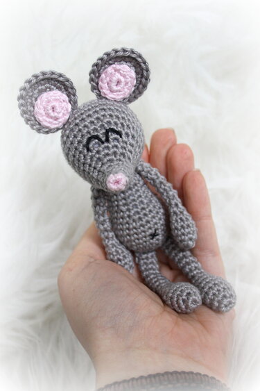 Hand hält kleine gehäkelte Amigurumi‑Maus in Grau mit rosa Ohren