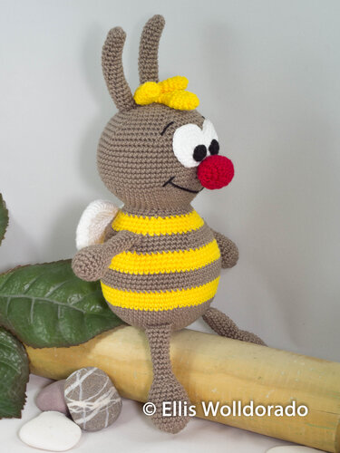 Gehäkeltes braun-gelbes Bienen‑Amigurumi sitzend mit roter Nase und weißen Flügeln