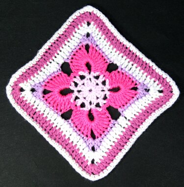 Mehrfarbiges gehäkeltes Quadrat mit zentraler Blüte in Pink, Lila und Weiß auf schwarzem Hintergrund