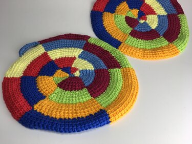 Zwei runde gehäkelte Topflappen in bunten Segmentringen, einer mit Aufhänger