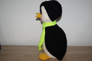 Gehäkelter Amigurumi-Pinguin, Seitenansicht, schwarzer Rücken, weißer Bauch, gelber Schnabel und Füße, leuchtgrüner Schal