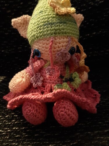 Pastellfarbene Amigurumi-Puppe mit kleinen Ohren, grüner Mütze und Häkelblumen