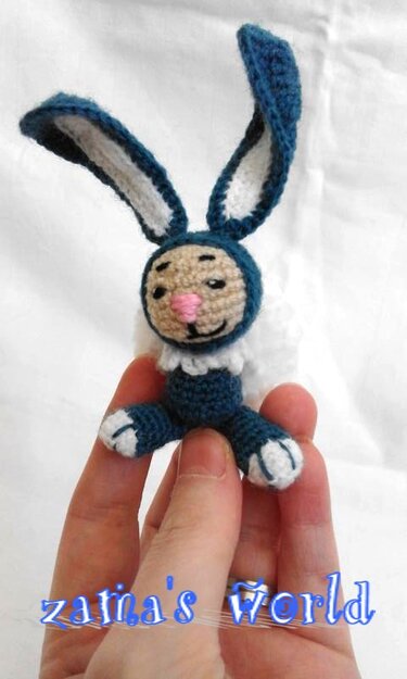 Hand hält kleinen gehäkelten Amigurumi-Hasen in Dunkelblau, Beige und Weiß